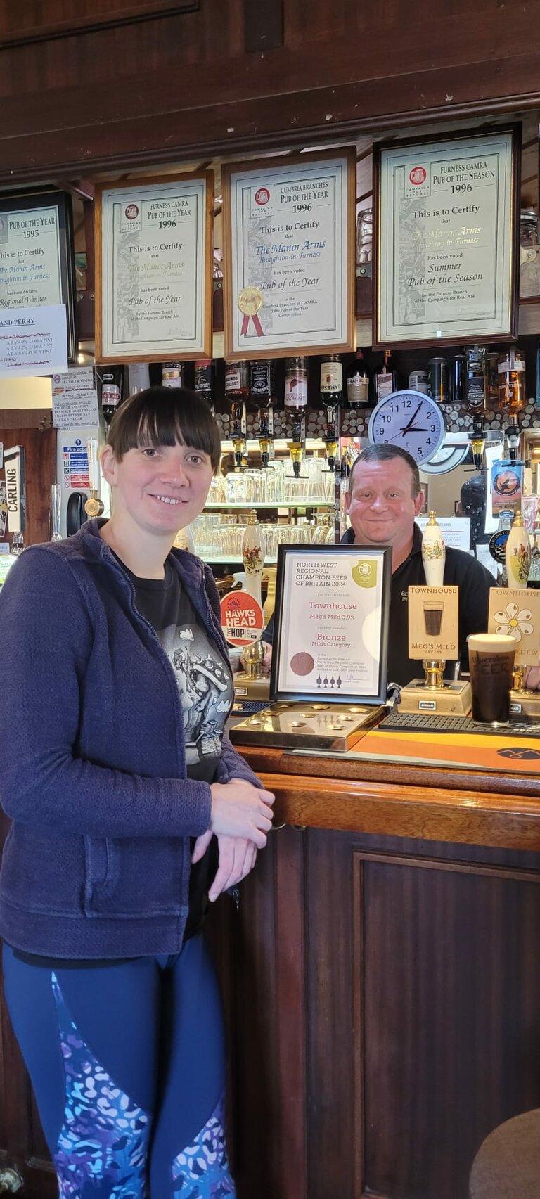 Megan Dixon, Mark the Brewer's partner, with the certificate for Meg's Mild, Bronze award in the Milds Category in the North West Regional Champion Beer of Britain, 2024 (with Scott Varty in the Background at The Manor Arms in Broughton).