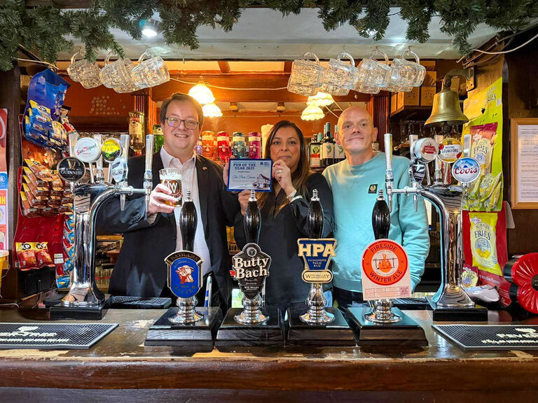 Bea and James Lane with Mr Wood and the award, behind the bar.